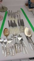 Complete set of assorted mother of pearl handled cutlery with silver plated parts arranged on a surface.