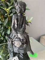 Front-left angled view of the statue showing the woman's face, basket, and detailed clothing with a background plant.