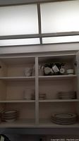 Cabinet showing stacked dinnerware pieces including plates and bowls, and teacups hung and stacked.