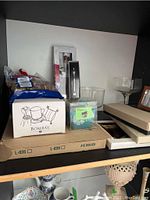 Wide shelf view showing boxed items including Bombay heart-shaped candle and several clear glass bowls and trays.
