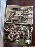 Silver plated cutlery laid out in divided trays showing assortment of forks, spoons, knives, and serving pieces with decorative handles.