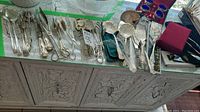 Overview of multiple silver plate serving utensils displayed on a cabinet