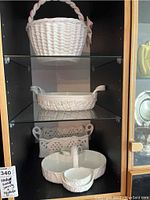Photo shows four Wedgwood ceramic baskets and server arranged on shelves inside a display cabinet.