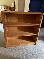 Front view of the wooden bookcase showing three shelves and visible scratches on the surfaces.