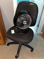 Black rolling office chair with Vornado fan sitting on the seat, showing general condition and items included.