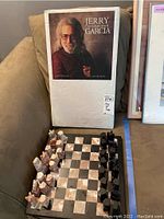 Full view of sealed white box with printed label “Jerry The Collected Artwork Garcia” alongside laid-out chess board and pieces