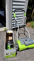 Green Works electric dethatcher alongside open box containing battery and charger