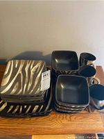 Overview of stacked square dinner plates, bowls, and coffee mugs with zebra pattern.