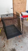 Black metal wire dog crate with a removable plastic tray set on the floor.