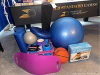 Fitness gear including Gaiam balance ball in original package, large blue exercise ball, basketball, Simply Fit exercise board, three foam rollers, and various accessories.