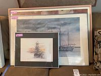 Three framed maritime and floral pictures stacked against a couch, showing relative sizes and framing.