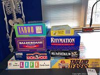 Photo showing stacked boxes of board games including Taboo, Balderdash, Rymation, Monopoly, Life, Rummikub, Tabloid Teasers, Krazy Bee Rummy