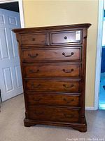 Front view of the wood highboy dresser showing seven drawers with metal handles and dark finish.