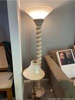 Full view of the floor lamp with twisted white column and frosted round glass shade next to a beige couch and chair.