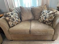 Front view of light beige loveseat with two geometric patterned throw pillows placed on it, showing overall condition and style.