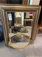 Large rectangular mirror with ornate gold carved frame standing on the floor. Beveled edges visible. Shows wear and chips. Reflection shows room.