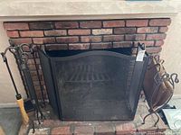 Full view showing fireplace screen, log holder, toolset with brush, and fire grate inside fireplace.