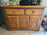 Front view of oak sideboard cabinet showing two drawers above and three doors below with wood grain patterns.