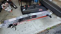 Two pairs of Salomon Snowscape 7s cross-country skis, one pair L183 and one pair LXXL193, stacked along with ski poles and a plastic ski carrier.