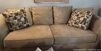 Front view of light beige 3-seat sofa with two patterned throw pillows on each end.