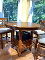 Photo of wood high top round table in a corner near windows, surrounded by chairs.
