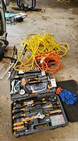 Wide view of tool cases open with yellow and orange extension cords coiled on floor, blue gloves, and other tools around