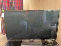 Front view of Panasonic 60-inch plasma TV turned off, showing screen reflections and black bezel with the silver base stand beneath.