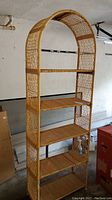 Front view of tall wicker shelf unit showing five shelves and arched top