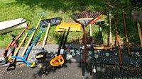 Wide view of all yard and garden tools laid out on ground showing variety of rakes, shovels, snow shovels and netting