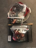 Overall view of the baking items stacked and arranged on the floor, showing silicone bakeware, cooling racks, rolling pins, and plastic bags with cookie cutters.