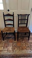 Photo showing two antique wooden chairs against a door background, one with a woven rush seat and the other with a wooden seat.
