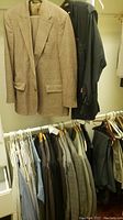 Photo showing multiple dress jackets and shirts hanging in a closet, focused on a light brown plaid blazer in front.