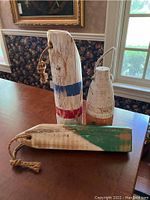 Three decorative wooden buoys of varying shapes and paint patterns on a wooden table, showing wear.