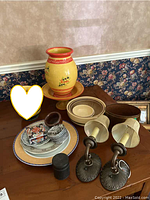 Overview of ceramic plates, bowls, a large yellow pitcher with a matching saucer, and two wall sconces with fabric shades.