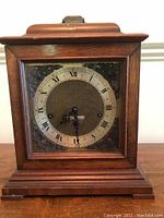 Front view of the clock highlighting the wood cabinet and ornate clock face with Roman numerals.