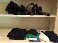 Four pairs of leather boots on the upper shelf, folded pants and tops placed on the lower shelf in various colors.