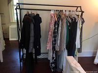 Full view of black metal clothing rack filled with various garments on hangers including coats and dresses, showing the structure and wear of the rack.