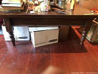 Full front view of a vintage dark wood coffee table showing turned legs, solid apron, and scratches on the surface.