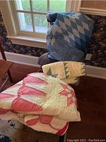 Four assorted quilts draped on chairs by window, showing colors and styles including blue and pink hues.