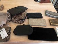 Photo shows a collection of various clutch bags and pouches arranged on a wooden table including leopard print and velvet clutches.
