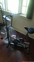 Side view of Schwinn Airdyne exercise bike showing large fan wheel, seat, and dual-action handles.
