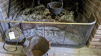 Metal mesh fireplace surround with brass top rail, cast iron ash bucket with wooden handle, and brass trivet placed inside surround
