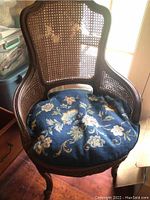 Full view of a dark wood French style chair with cane back and sides, showing the curved frame, cane webbing damage, and needlepoint floral cushion on seat.