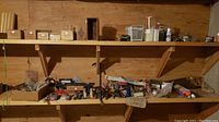 Wide view of wooden shelves with multiple boxes and containers holding tools and hardware items such as bolts, screws, nails, and painter's supplies.