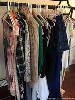 Photo showing a side view of the clothing rack with floral dresses, a faux fur vest, plaid skirt or slacks, and various tops and shirts hanging on hangers.
