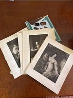 Set of 16 black and white lithographs shown stacked on a wooden surface with hardcover book on Scottish woodware behind them