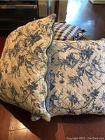 Side view of a floral pillow and checked cushion stacked on each other showing item's thickness and pattern.