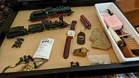 Overview of shadow box case with assorted collectibles including miniature trains, wristwatch, pins, and other small items