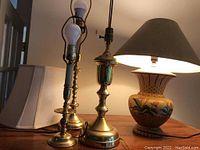 Four table lamps: three with brass bases and one painted ceramic floral base with a black shade. Also visible two light bulbs are mounted on two brass lamps.