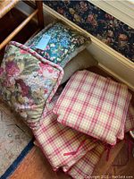 Four throw pillows stacked together showing different floral and patterned fabric covers in various colors including pink, green, beige.